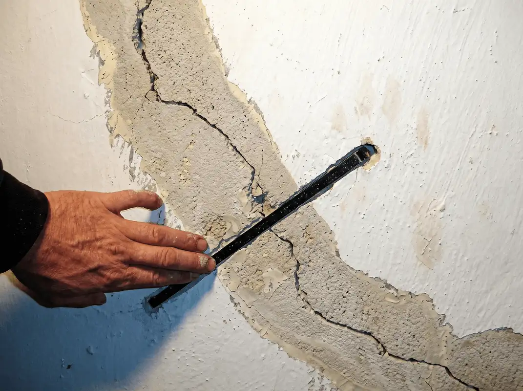A wall with a large crack is being inspected by a professional in Akron, OH