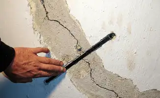 A wall with a large crack is being inspected by a professional in Akron, OH